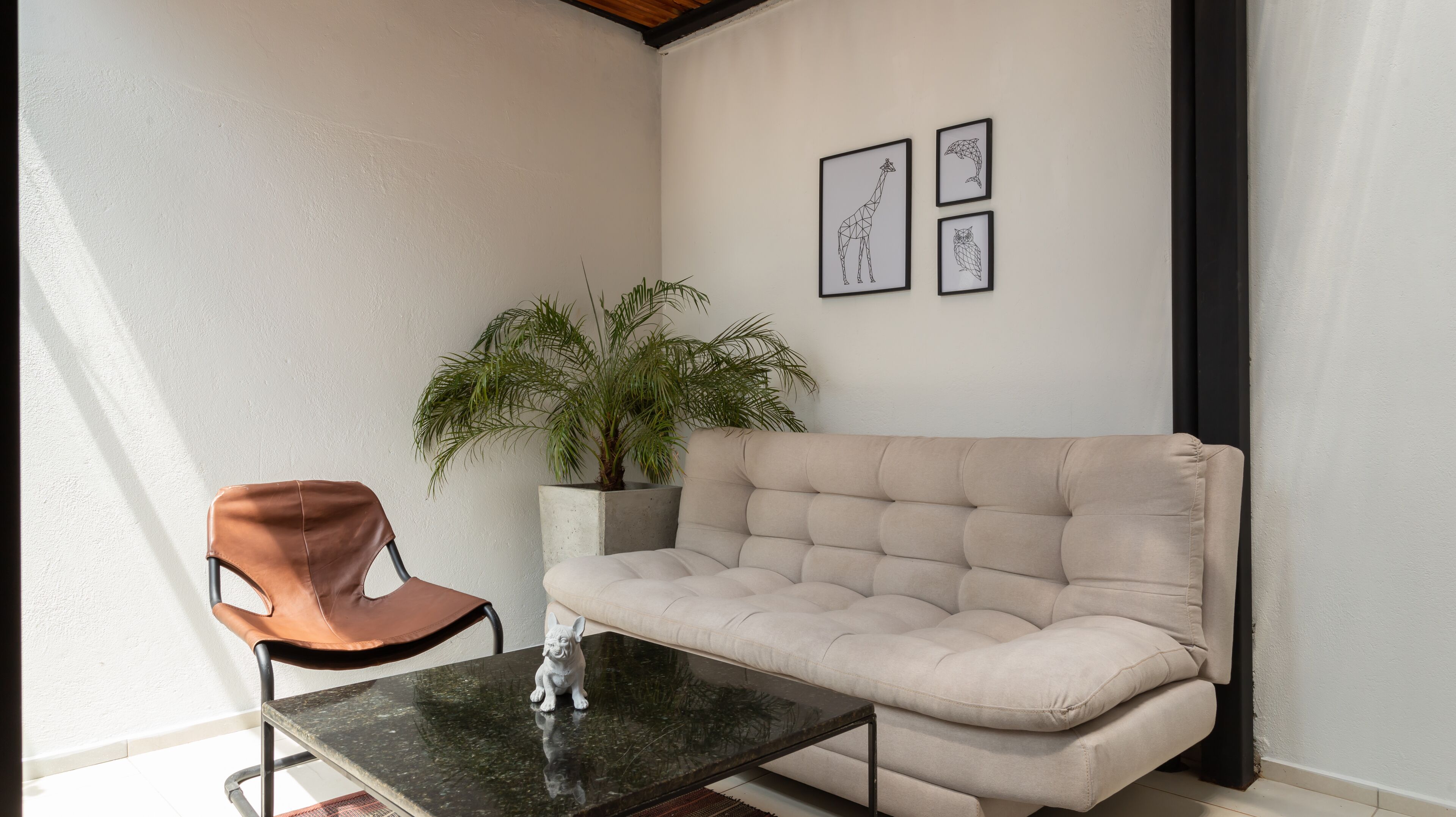 Ein Eckzimmer mit einem beigefarbenen Sofa, einem braunen Ledersessel, einem kleinen Tisch und einer Topfpflanze.