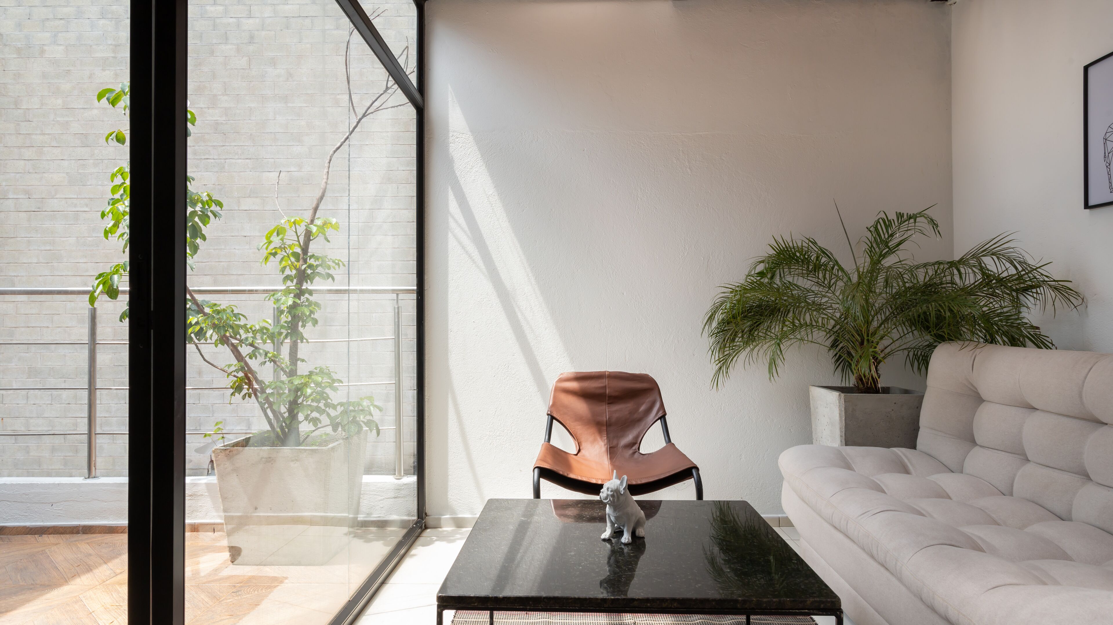 Ein modernes Wohnzimmer mit Glastür zum Balkon, ein Ledersessel, eine Couch und zwei Topfpflanzen.