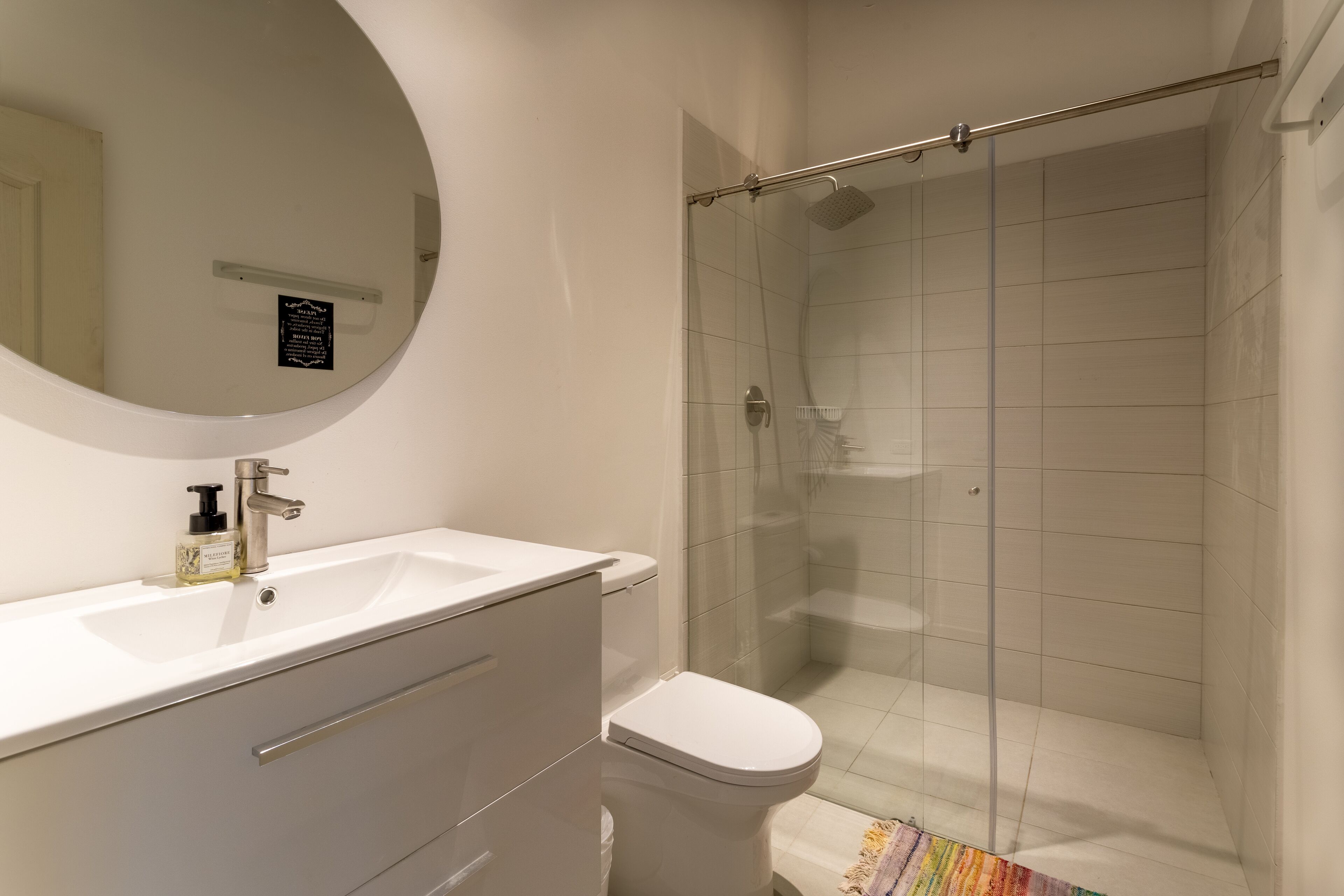 Een badkamer met een wit wastafel, een spiegel, een toilet en een douche met glazen wanden.