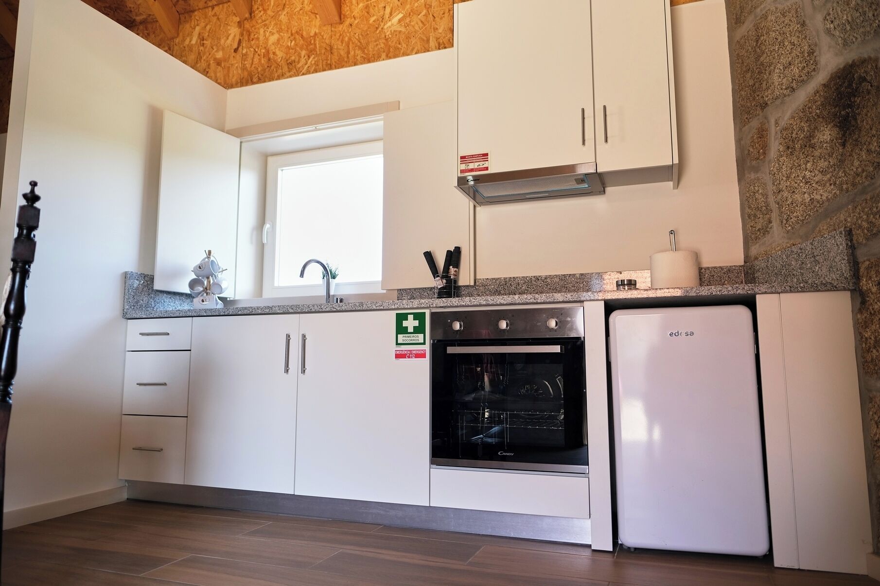 Una cucina con mobili bianchi, forno a incasso, frigorifero bianco e una finestra sopra il lavello.