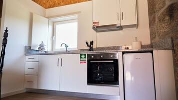 Una cucina con mobili bianchi, forno a incasso, frigorifero bianco e una finestra sopra il lavello.