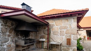 A stone building with a tiled roof, a stone wall, and a metal grill area.
