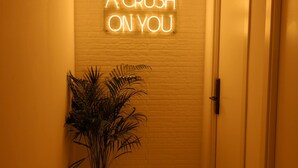 Um corredor com um letreiro de neon que diz 'I HAVE A CRUSH ON YOU' na parede, um vaso de planta e uma porta.