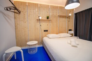 A modern hotel room with a wooden wall panel, a bed with white linens, a small round table, and a hanging lamp. - Koala Hostel Mercado (Alicante)