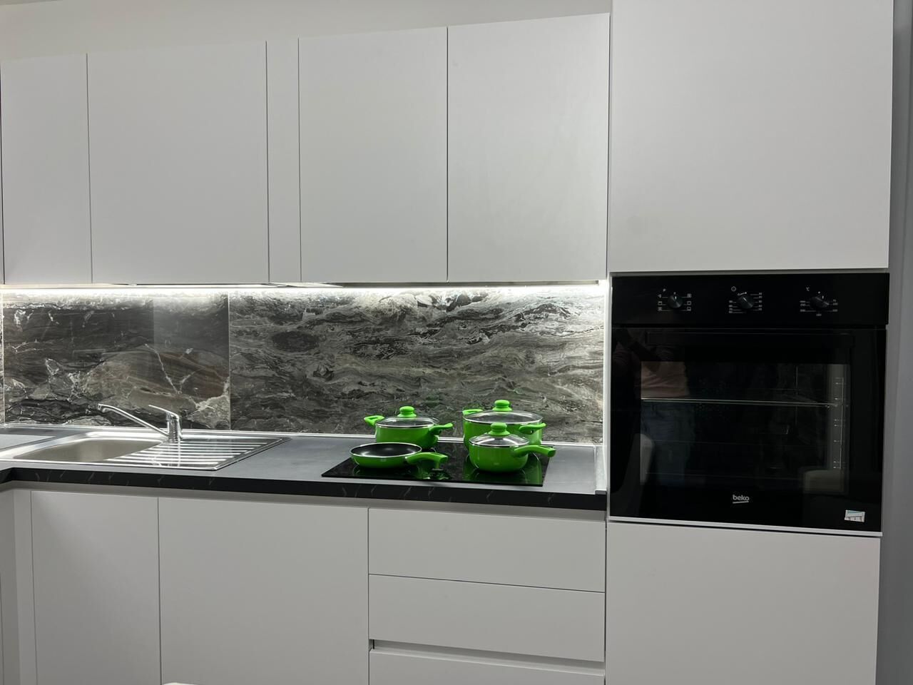 Eine moderne Küche mit weißen Schränken, einer schwarzen Arbeitsplatte und einem eingebauten Backofen.