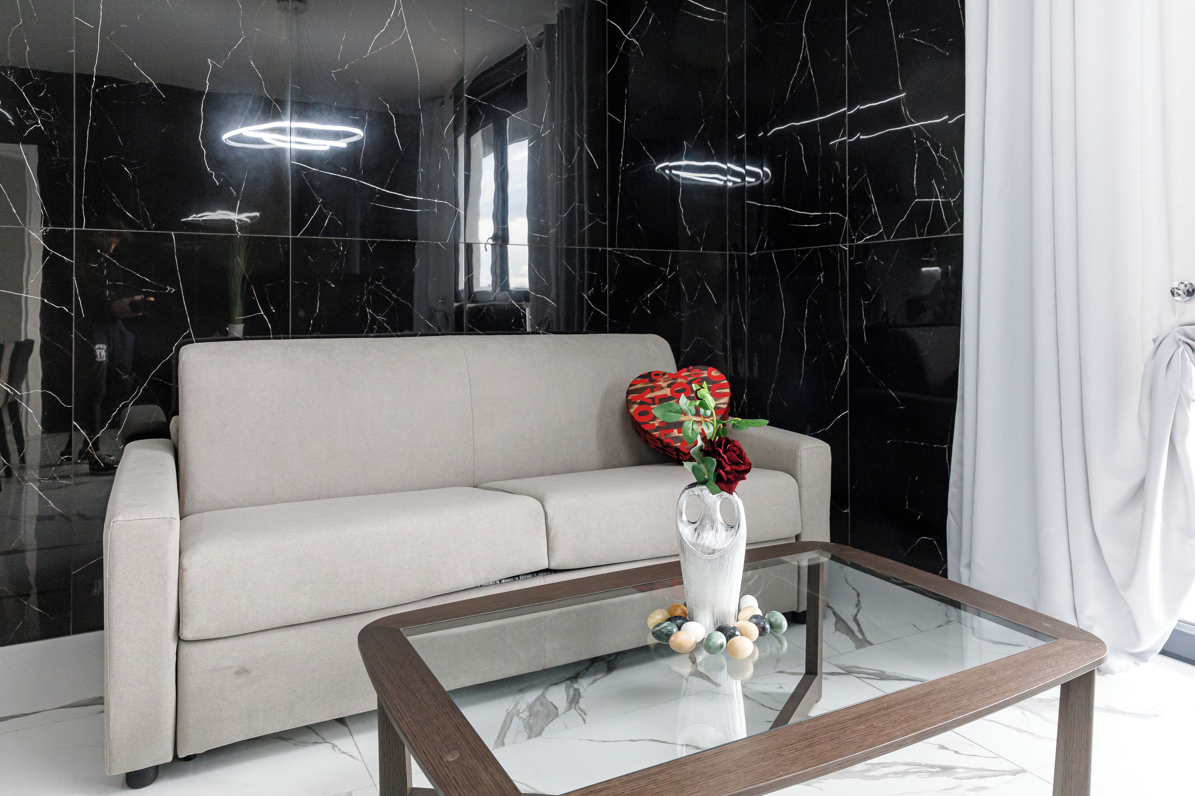 Un salón moderno con suelo de mármol, una mesa de centro de cristal, un sofá y un jarrón con flores.
