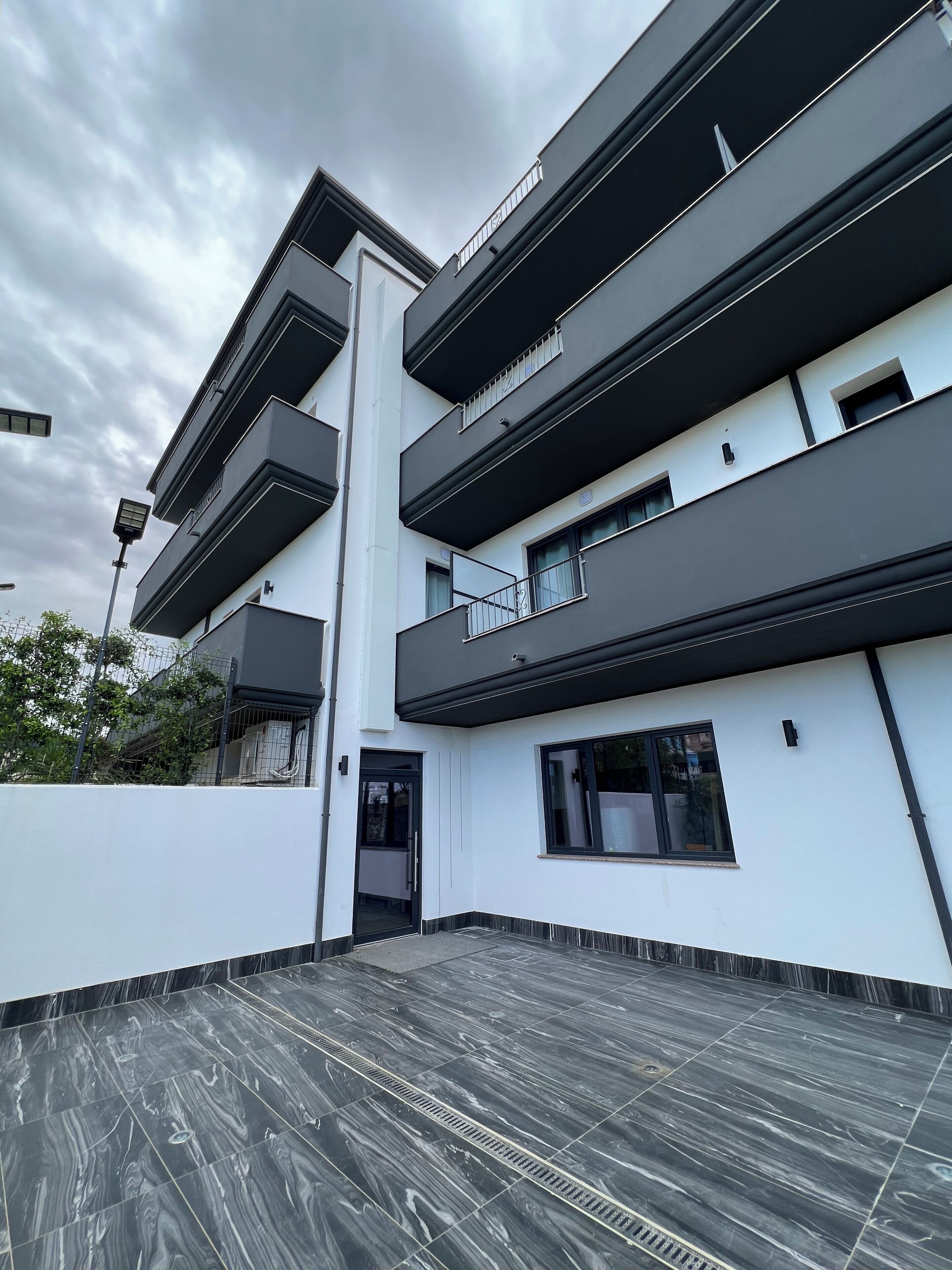 A modern multi-story building with balconies, a flat roof, and a paved terrace.