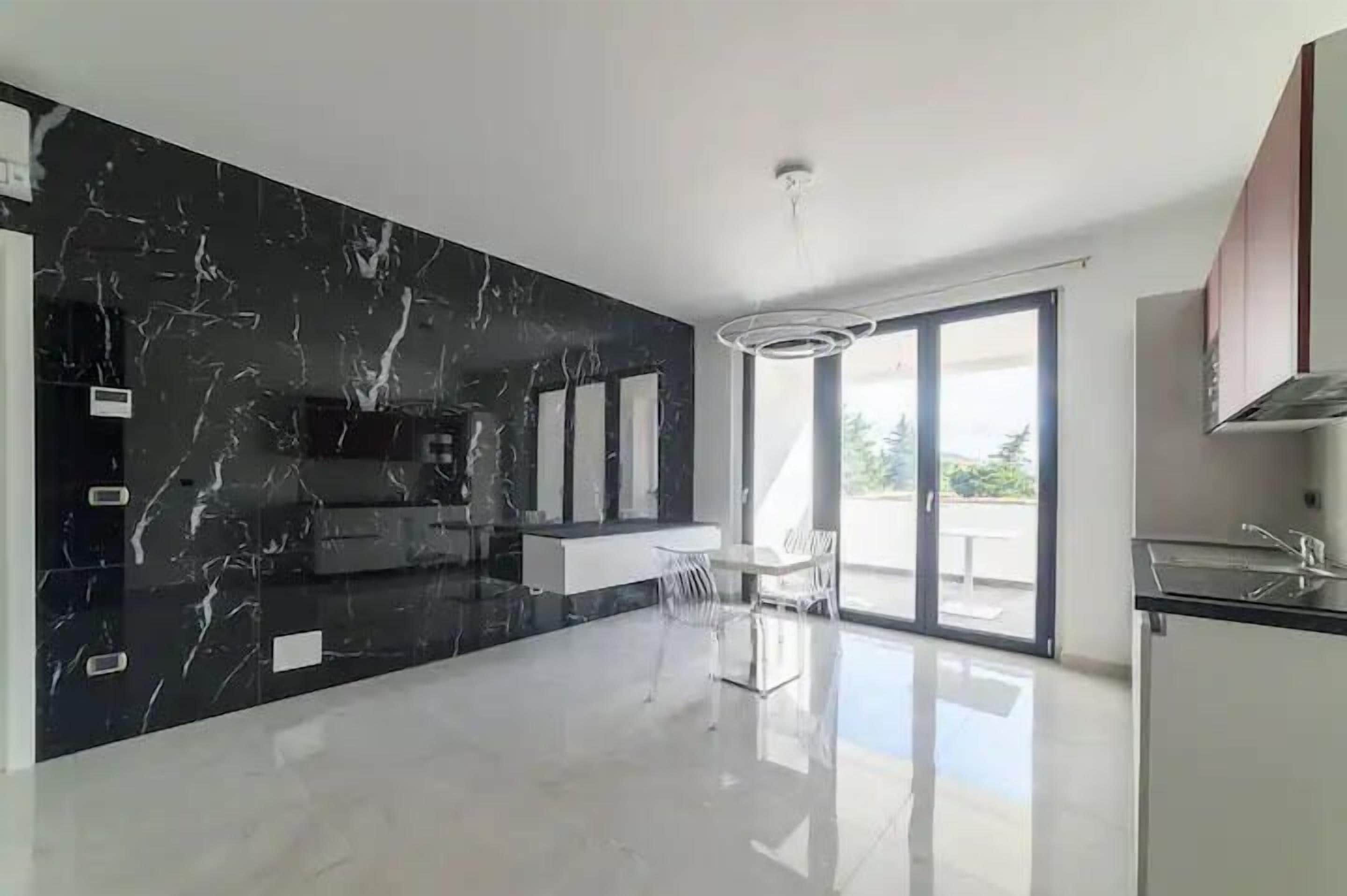 A modern kitchen with a black marble backsplash, a central island, and a dining area with a glass table and chairs.