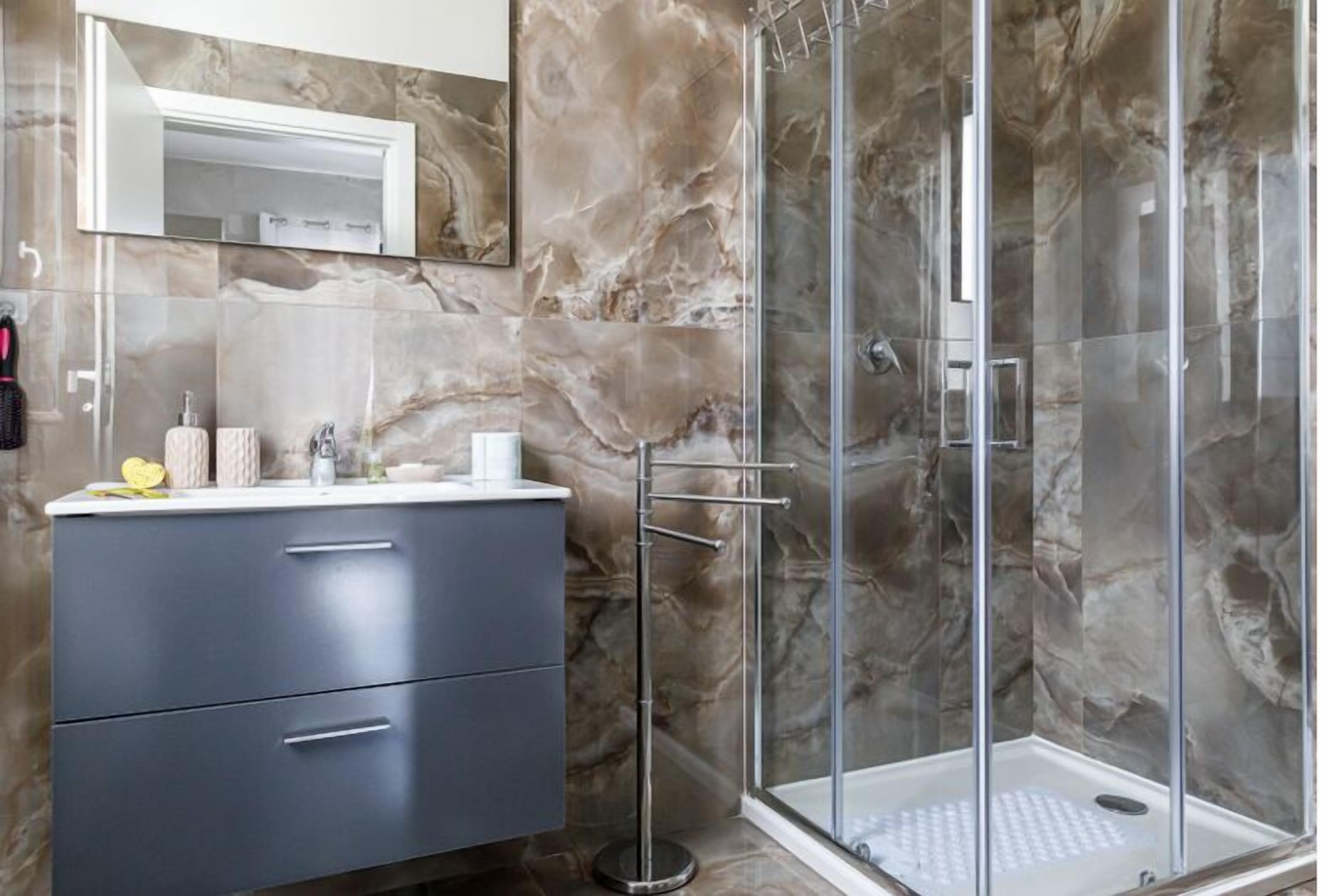 Une salle de bain moderne avec une douche à l’italienne en marbre, un meuble-lavabo avec miroir et un porte-serviettes.