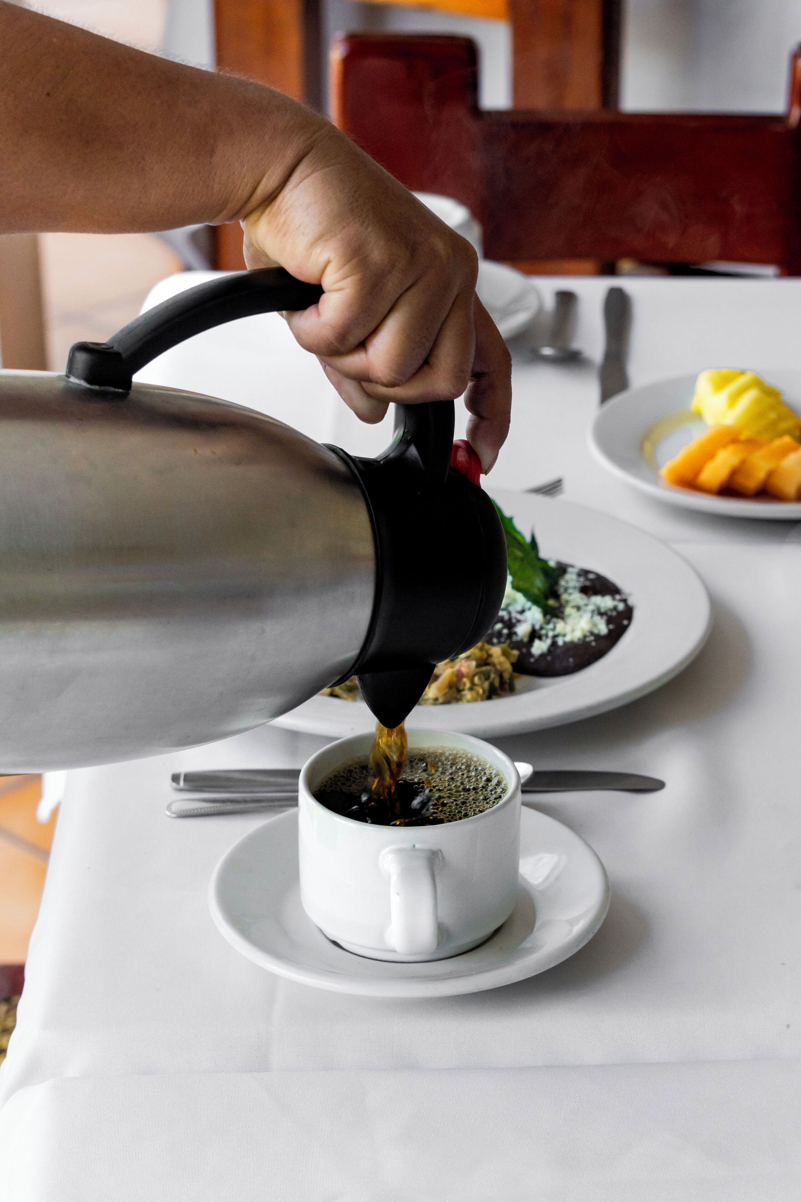 Une main verse du café d’une théière dans une tasse posée sur une soucoupe.