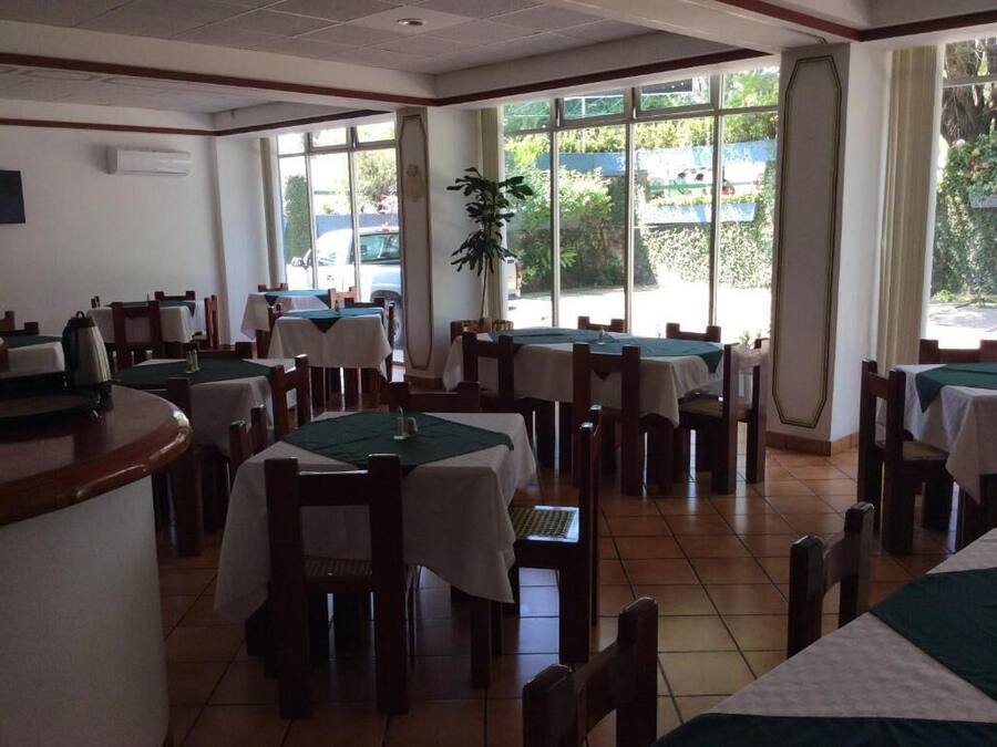 Un restaurante con varias mesas y sillas, ventanas amplias y una planta en el centro.