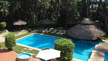Ein Swimmingpool mit Liegestühlen und Strohsonnenschirmen, umgeben von üppiger Vegetation.