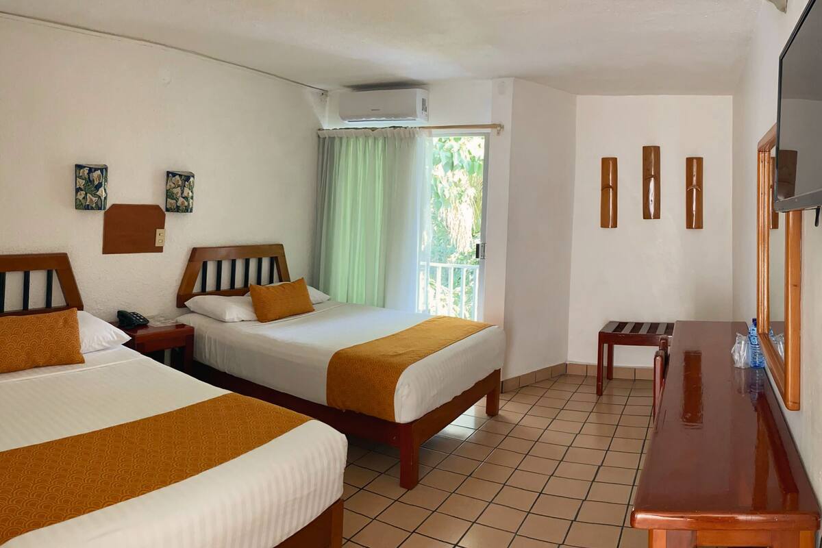 Habitación de hotel con dos camas, un escritorio, una silla, un televisor y un balcón con cortinas.
