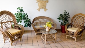 Ein Zimmer mit Korbmöbeln, einem kleinen Tisch mit Blumen in einer Vase und Topfpflanzen.