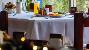Ein Esszimmertisch mit Tellern, einer Karaffe und einem Glas Saft, umgeben von Stühlen und einer großen Pflanze.