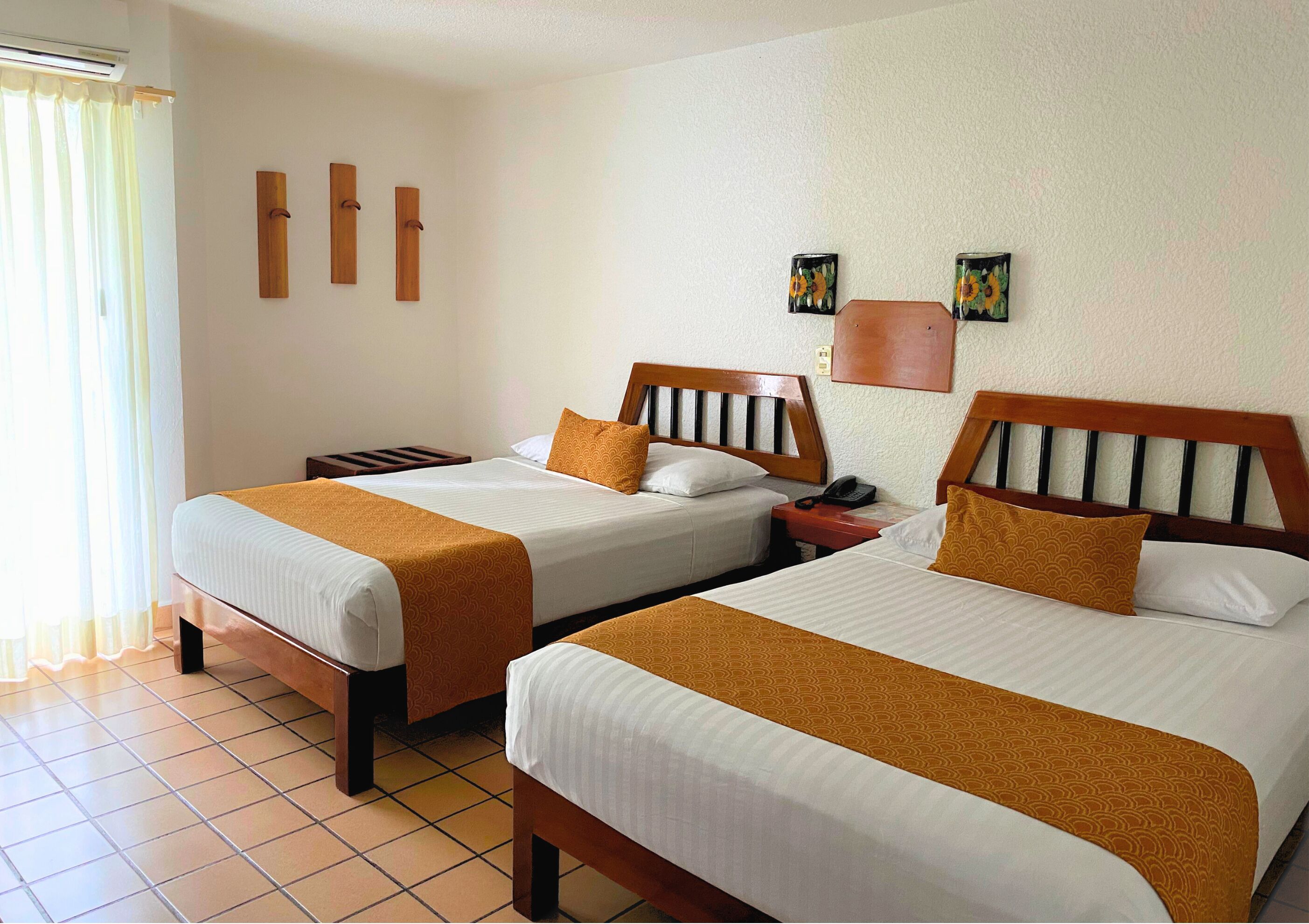 A hotel room with two beds, a nightstand, a wall-mounted phone, and a window with curtains.