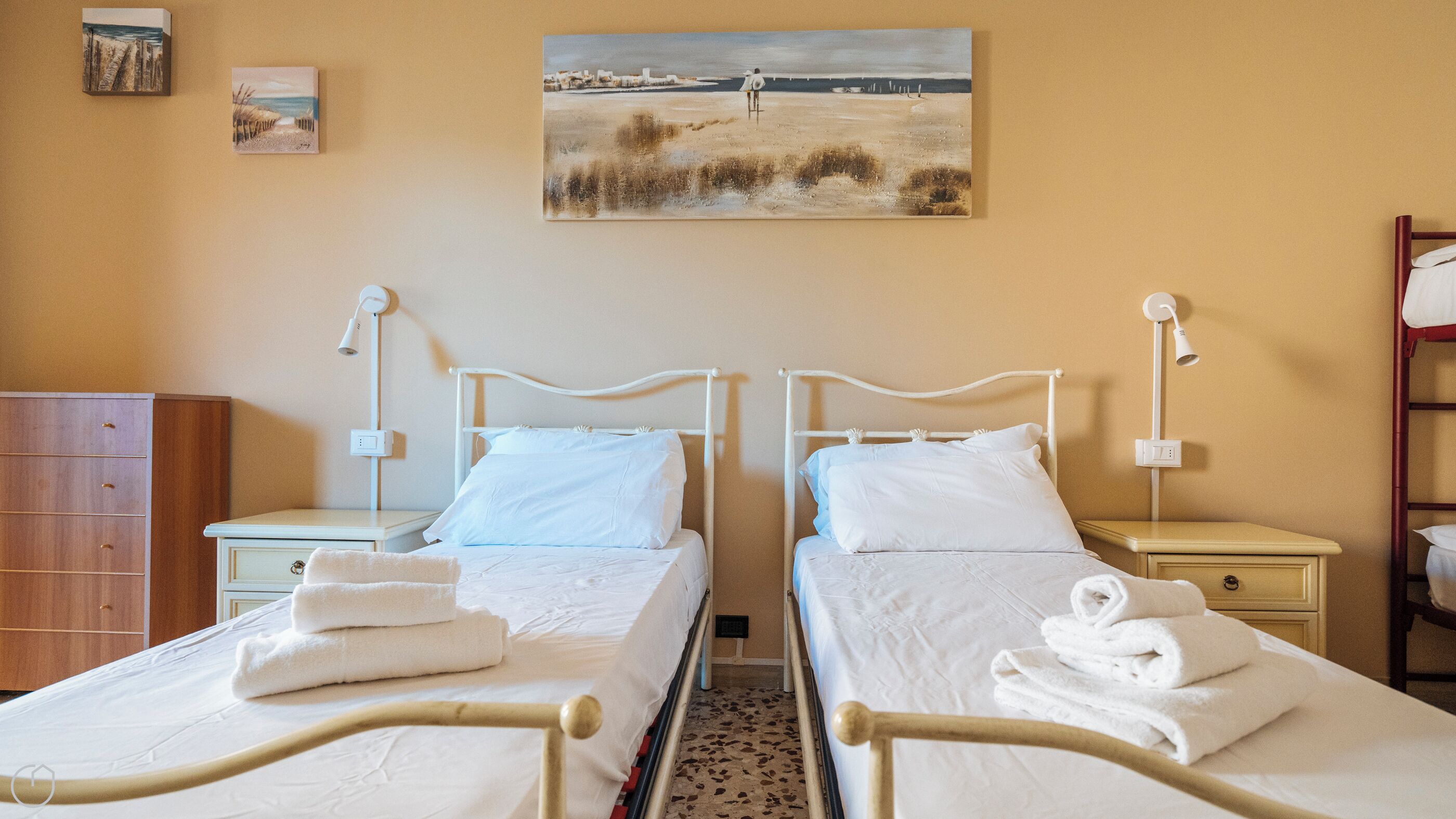 Habitación de hotel con dos camas, lámparas de noche, un armario de madera y un cuadro de playa en la pared.