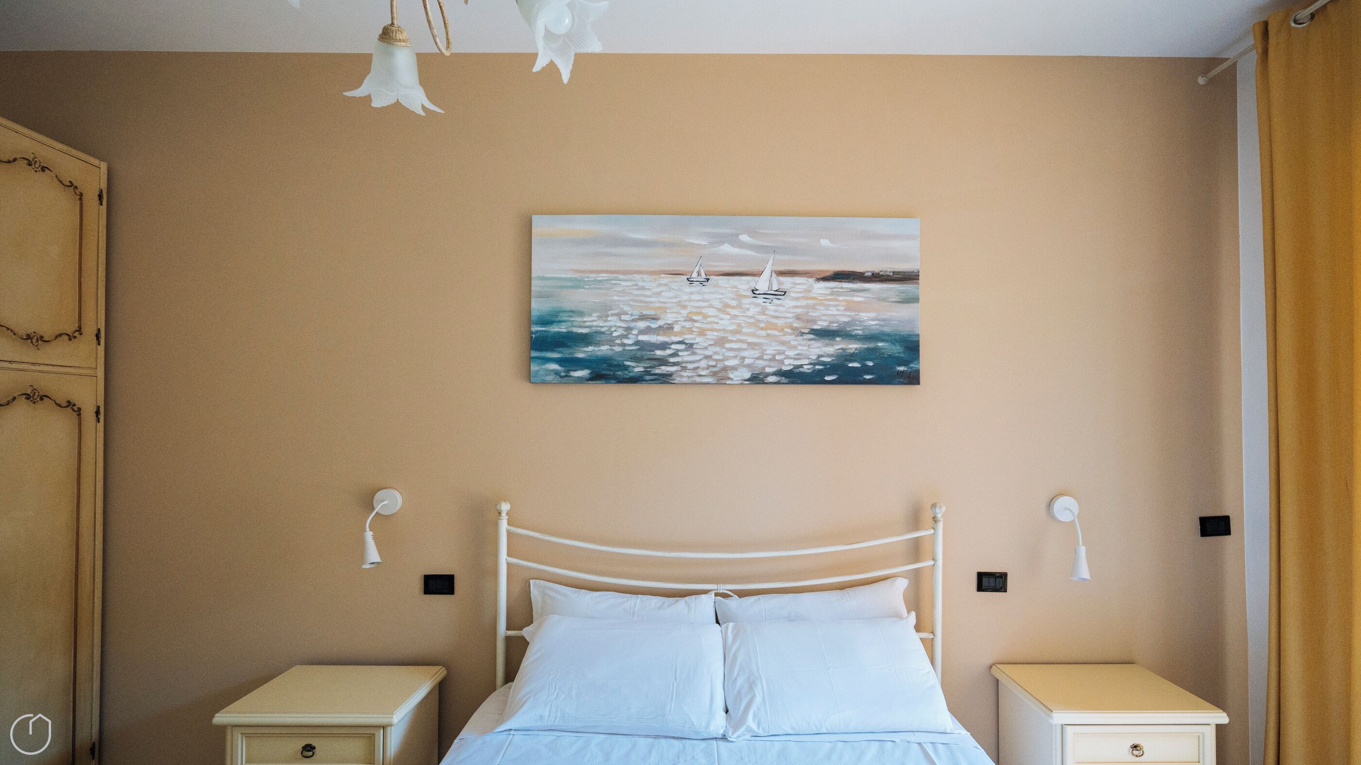 A bedroom with a bed, bedside tables, a painting of sailboats, and a light fixture.