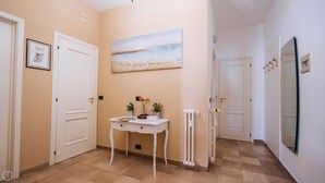 A hallway with a white door, a framed picture, a painting, a small table with a sign, and a radiator. - Marina Bike Family Home (Andora)