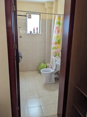 A bathroom with a toilet, a shower, and a window. - Eilarose City View Suites (Nairobi)