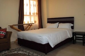 Uma cama bem arrumada com lençóis brancos, cabeceira marrom e uma pequena mesa de cabeceira.