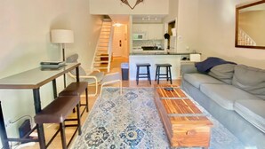 Un espace de vie compact comprenant un coin cuisine, un coin repas avec une table et des chaises, un canapé et un tapis à motifs.