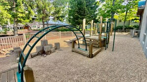 Une aire de jeux dotée de structures en bois et de structures métalliques vertes, entourée de gravier et d’arbres.