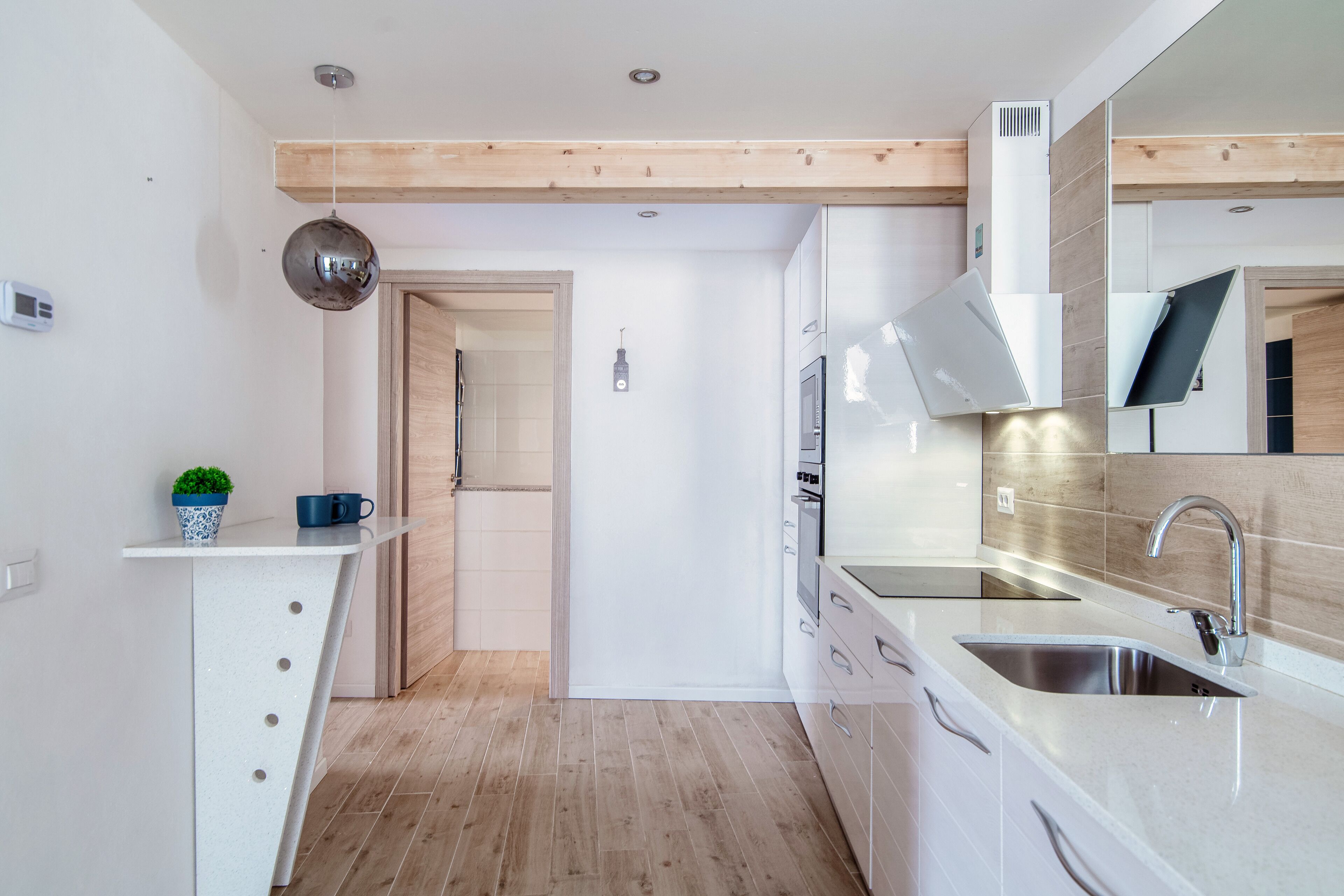 A modern kitchen with white cabinetry, a stainless steel sink, and a wooden ceiling.