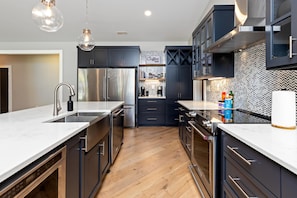 A modern kitchen with dark cabinets, stainless steel appliances, and a marble countertop.