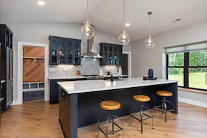 A modern kitchen with a large island, bar stools, and pendant lighting.