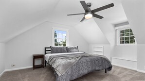 A bedroom with a sloped ceiling, a bed with gray bedding, a small bedside table, and a ceiling fan. - Waynesboro Home Near Wintergreen Charlottesville (Waynesboro)