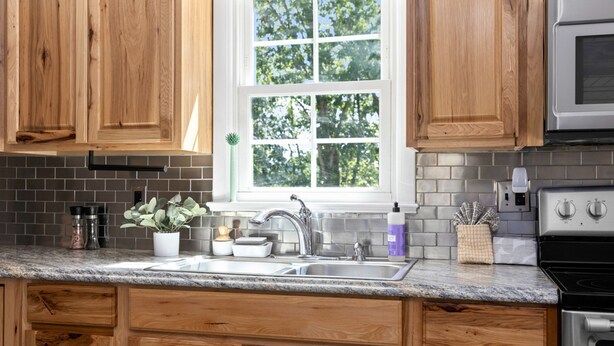 A kitchen with wooden cabinets, a granite countertop, a sink, a window with a view of trees, and a stove. - Waynesboro Home Near Wintergreen Charlottesville (Waynesboro)