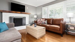 A living room with a fireplace, a brown leather sofa, a grey armchair, and a wooden coffee table. - Waynesboro Home Near Wintergreen Charlottesville (Waynesboro)