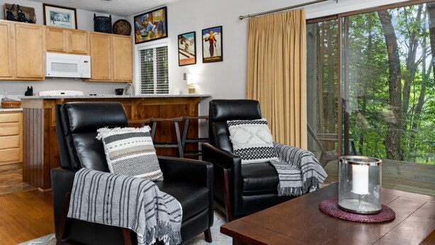 A cozy living room with two black leather chairs, a wooden coffee table, and a large window with a view of trees. - Condo at Wintergreen Walk to Slope Pool Access (Nellysford)