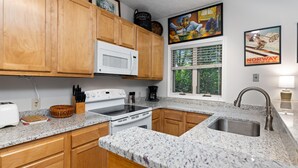 A kitchen with wooden cabinets, a white microwave, a stove, and a sink. - Condo at Wintergreen Walk to Slope Pool Access (Nellysford)