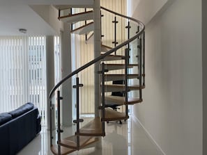 A modern spiral staircase with glass railings and wooden steps, leading to an upper floor. - Cosy 3 bed Penthouse in Royal Docks London (London)