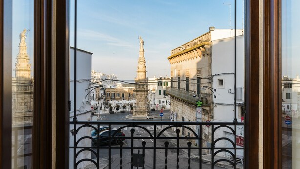 Blick aus einem Fenster auf einen Stadtplatz mit historischen Gebäuden und einem Denkmal.