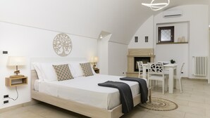 Ein Schlafzimmer mit einem Bett, Nachttischen, einer Lampe, einem Kamin und einer Essecke mit Stühlen.