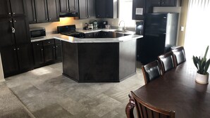 Une cuisine moderne avec des meubles de couleur sombre, un îlot central, des appareils en acier inoxydable et un coin repas comprenant une table et des chaises.