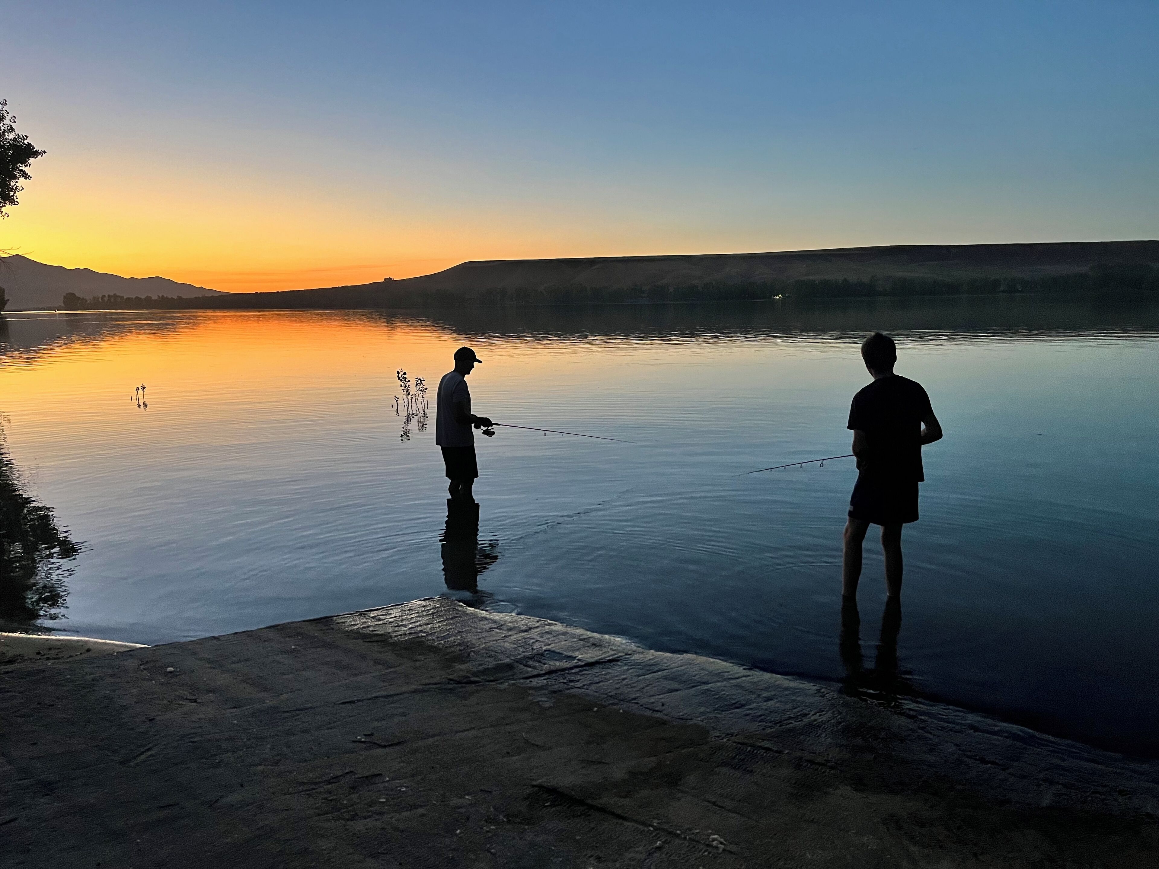 Deux personnes pêchant au bord d’un lac paisible, au coucher du soleil.
