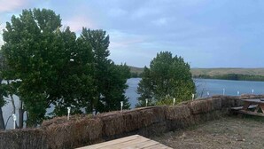 Une table et des bancs en bois, installés près d’un lac, entourés d’arbres et d’un mur de pierres sur lequel sont fixés des poteaux numérotés.