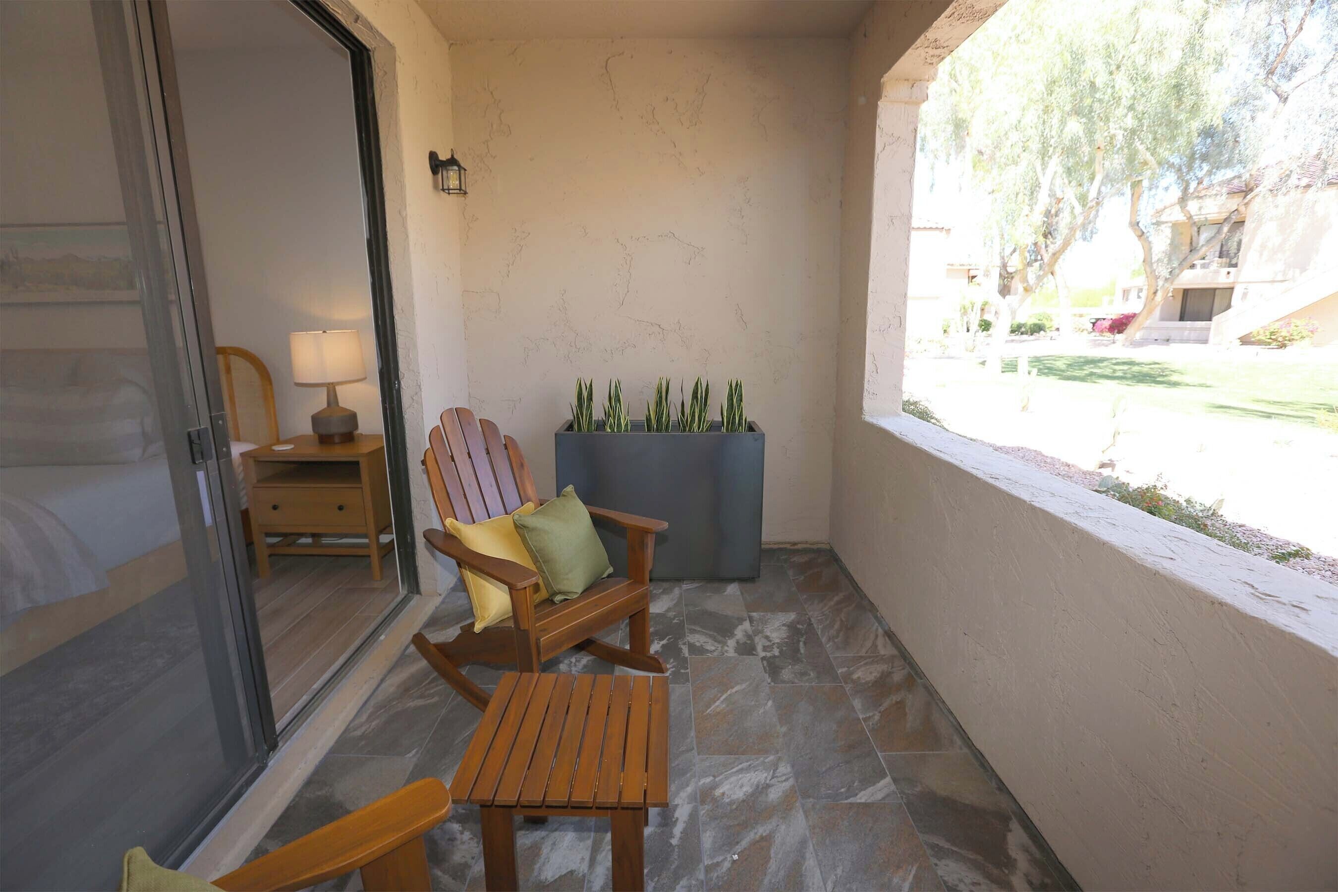 A balcony with a wooden chair, a small table, and a planter with green plants.