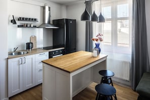 A modern kitchen with white cabinets, a wooden countertop, a black refrigerator, and a window with curtains. - Corner House Residence (Kraków)