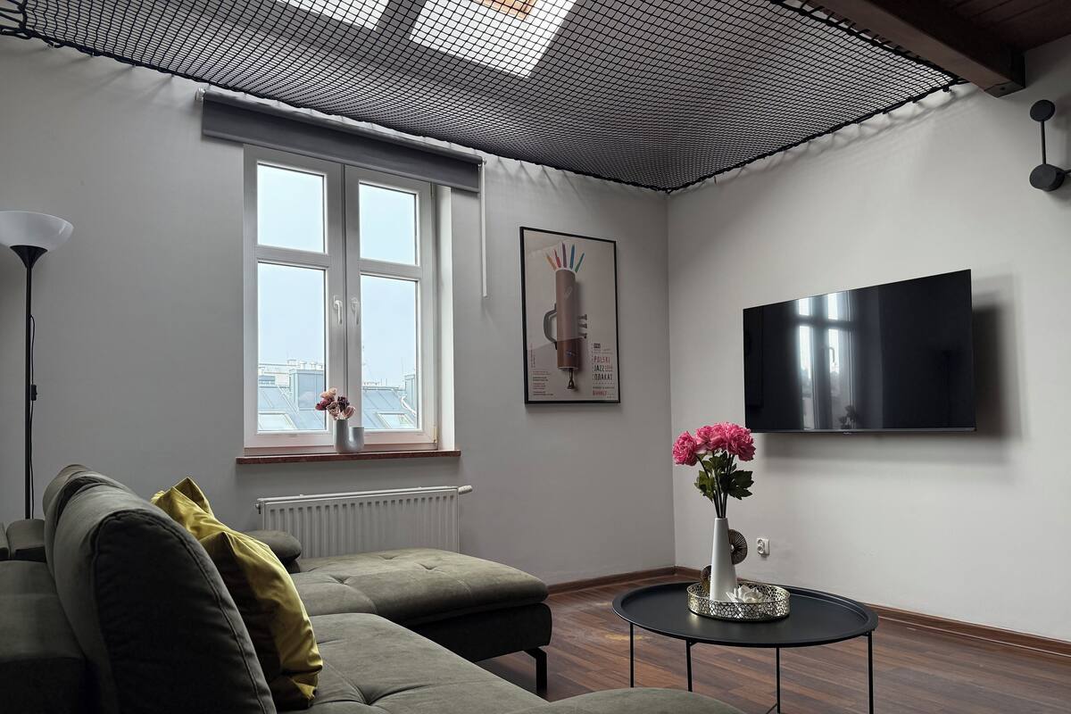 A modern living room with a sofa, a small table, a TV, and a window with a view of buildings.