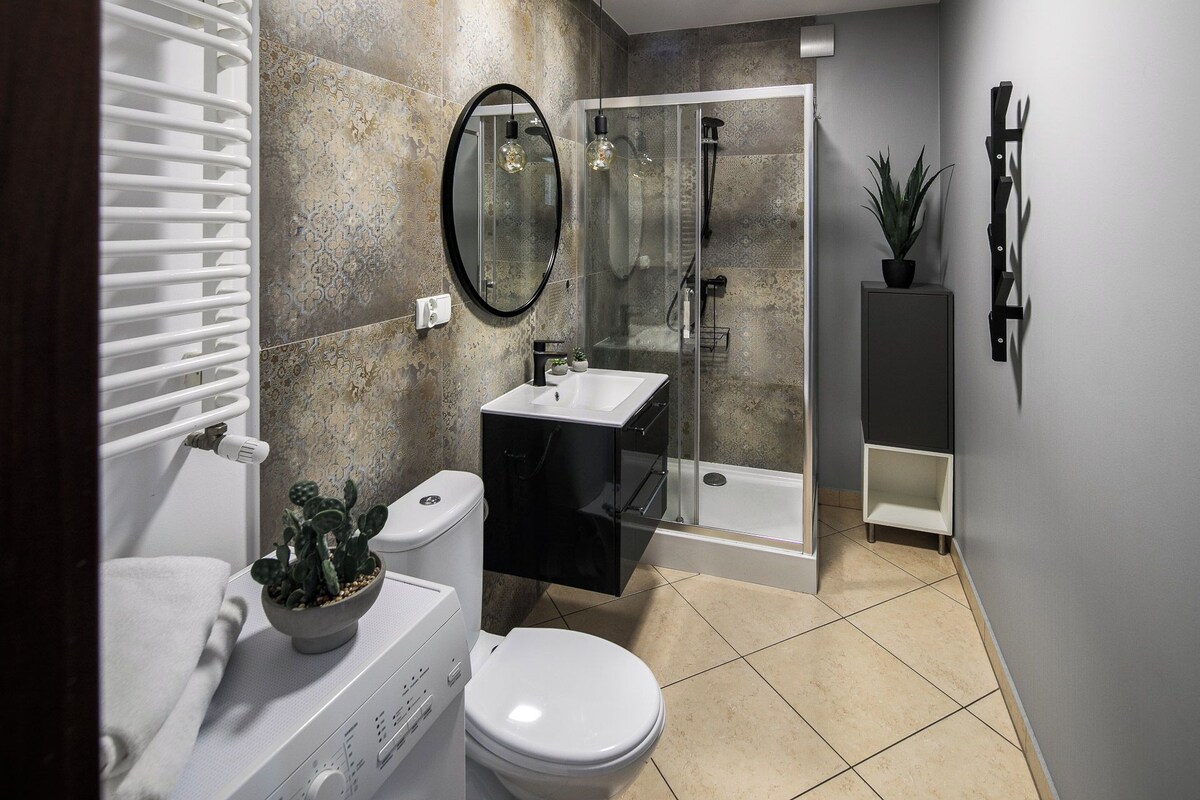 Un baño moderno con ducha de vidrio, inodoro blanco, lavabo negro y un espejo.