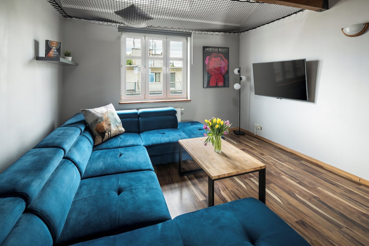A modern living room with a blue sectional sofa, a wooden coffee table, and a flat-screen TV mounted on the wall.
