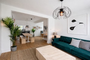 Een moderne woonkamer met een groene bank, een houten salontafel en een eethoek met een houten tafel en stoelen.