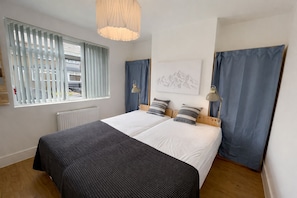 Een slaapkamer met een groot bed, twee nachtkastjes, een raam met zonwering, een radiator en een kunstwerk aan de muur.