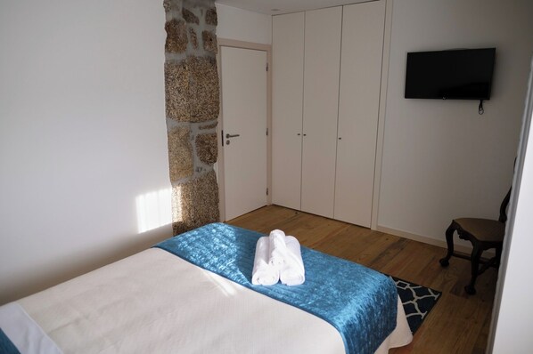 A bedroom with a bed, a stone wall, a wardrobe, a television, and a chair.