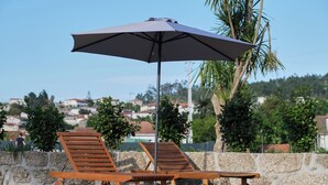 Twee houten loungesteunen op wielen, een parasol en uitzicht op een woonwijk met huizen en bomen.